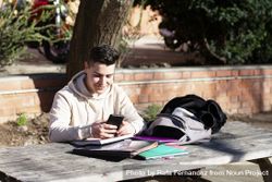 Young student sitting in a park while using a mobile phone on a wooden table bGRPZA