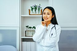 Curious Asian doctor thinking about something in her office