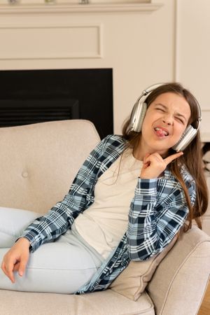 Playful girl making funny faces wearing headphones indoors.