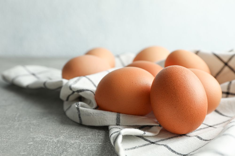 Brown chicken eggs in kitchen towel on grey table against light background, space for text and closeup
