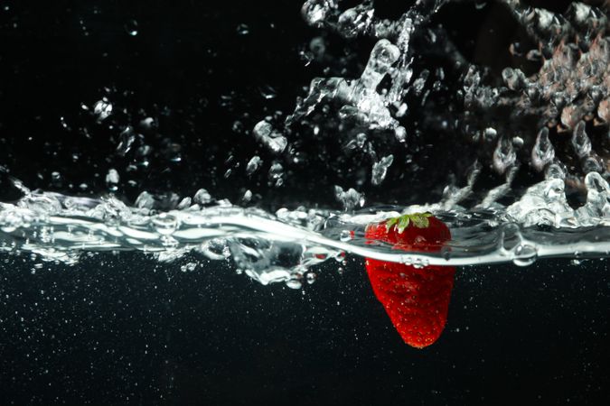 Side view of water splashing on dark background with strawberry