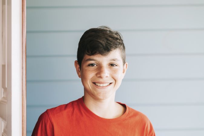 Portrait of happy male teen standing in doorway while looking at camera