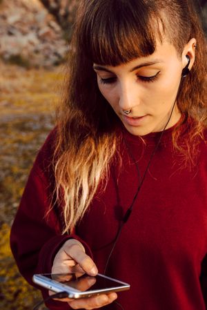 Young woman with piercing listening music on smartphone on hill