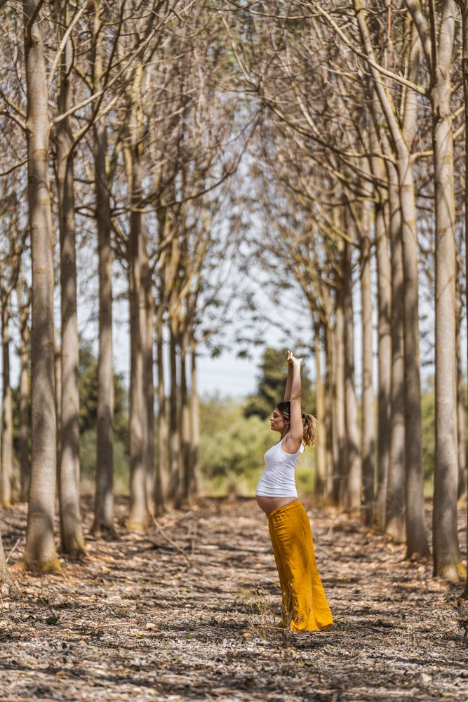 Adult expectant mother practicing yoga in park during sunny day