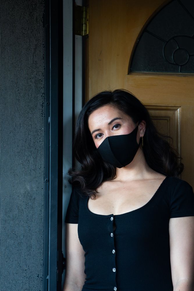 Portrait of woman standing in front of her home with PPE mask and dark dress
