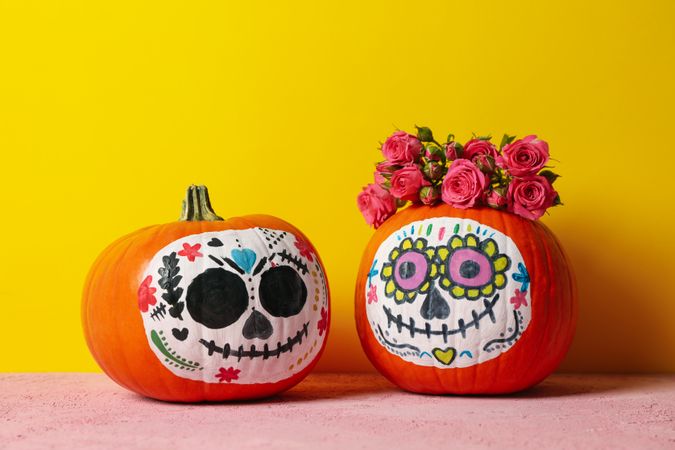 Pumpkins with catrina skull makeup and flowers on yellow background