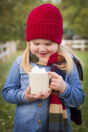 Cute Young Girl Holding Cocoa Mug with Marsh Mallows Outside