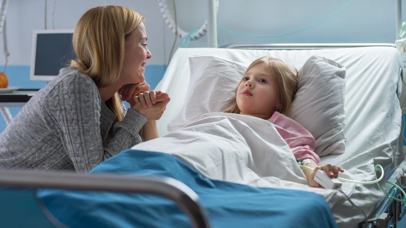 Cute Little Girl Lies on a Bed in the Children's Hospital, Her Mother Sits Beside, They Talk
