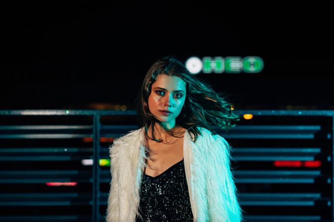 Female model in faux fur coat posing at night on a rooftop terrace