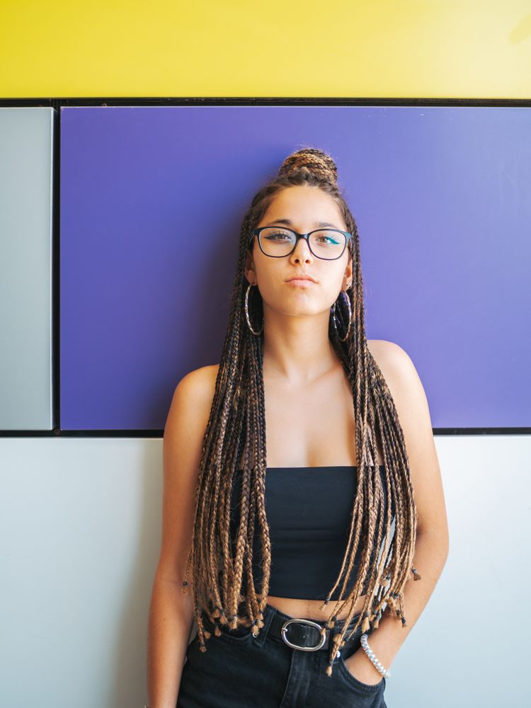 Charming teenage girl with braids in sunglasses nearby colorful wall