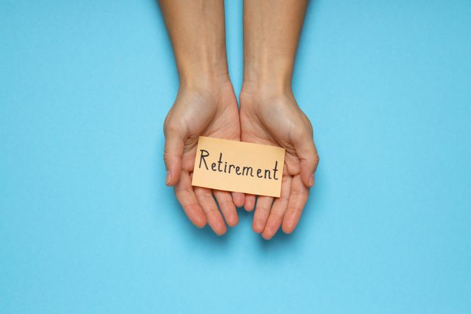 Female hands holding paper with text Retirement on blue background