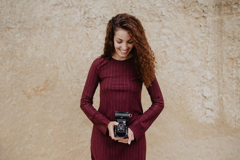 Cheerful woman with camera near rough wall