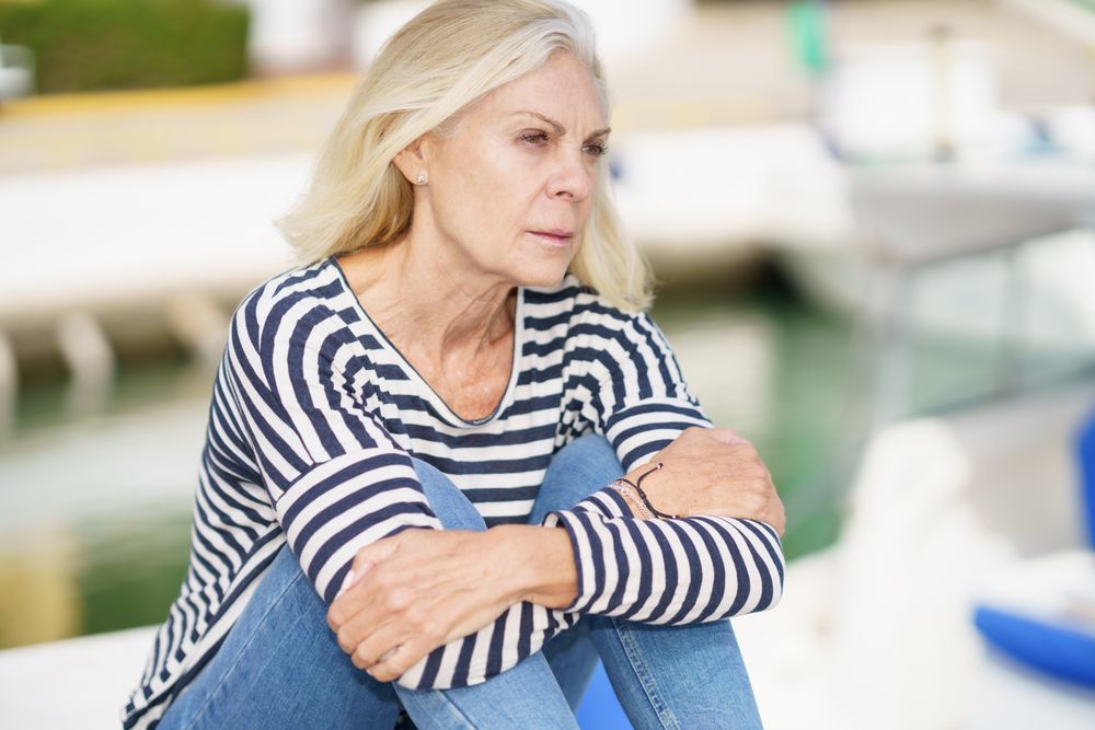 Portrait of older female deep in thought sitting on a pier on sunny day