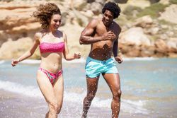Black man and white woman running playfully along the seashore