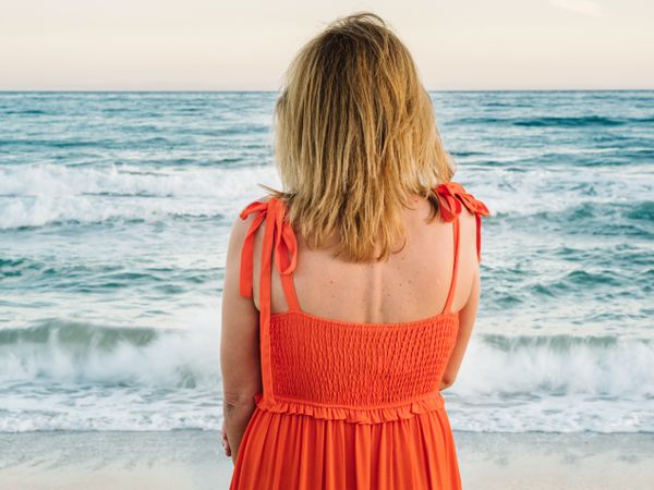 Woman in red dress looking along at seaside