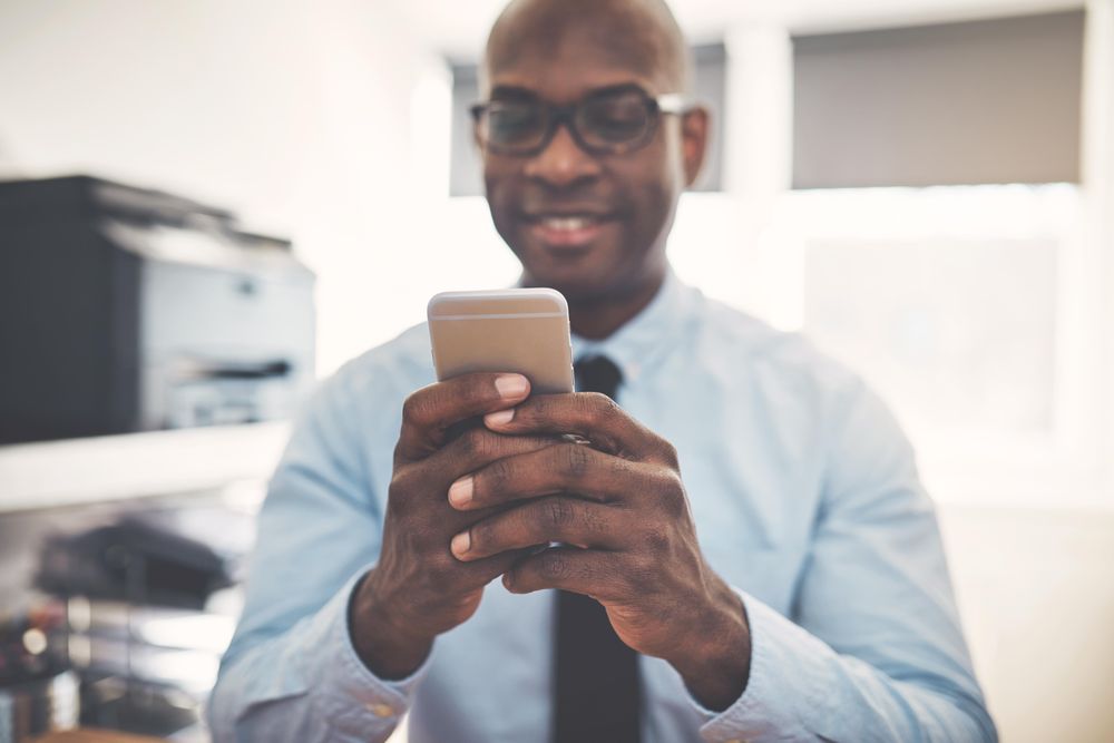 Man dressed in shirt and tie texting in home office