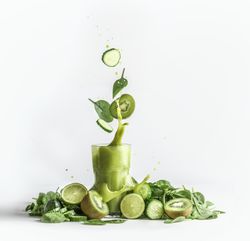 Splashing of green smoothie in glass with and flying ingredients: cucumber,kiwi and spinach leaves