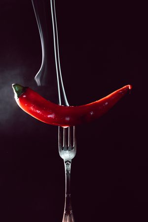 red chili pepper on fire in fork on a dark background