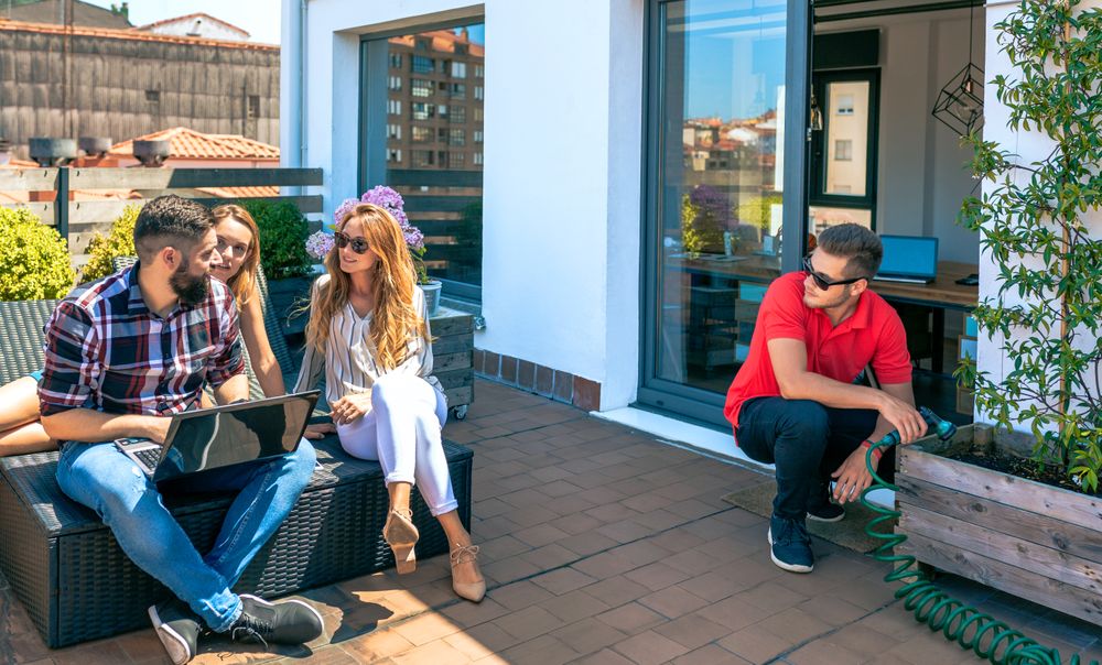 Colleagues talking in a coffee break while man watering plants in office rooftop