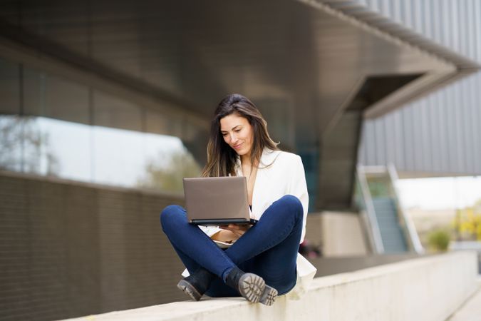 A Young Woman Concentrating While Working on a Laptop Outdoors in a Modern Urban Environment