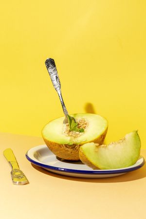 Sliced small melon on plate with spoon and fork