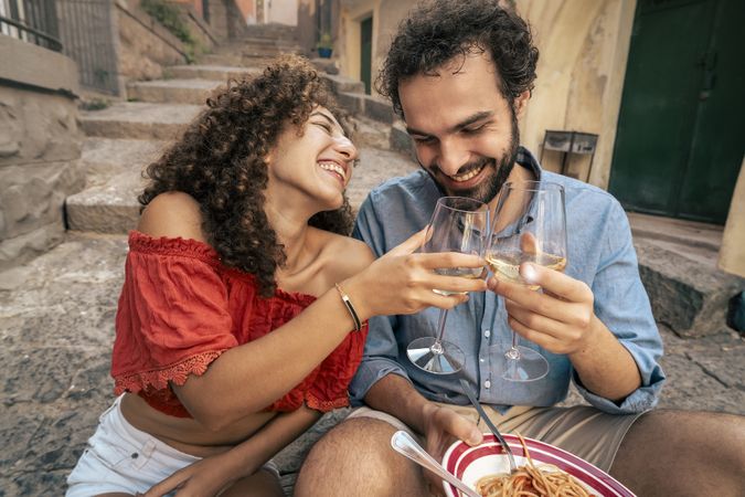 Happy couple toasting with wine and eating pasta in Italy