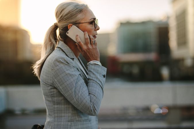 Mature businesswoman walking outdoors on street with mobile phone