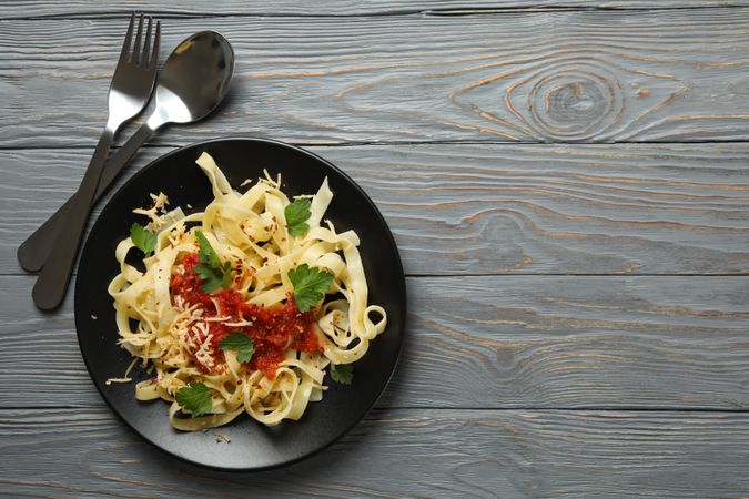 Cutlery and plate of tasty pasta on wooden background