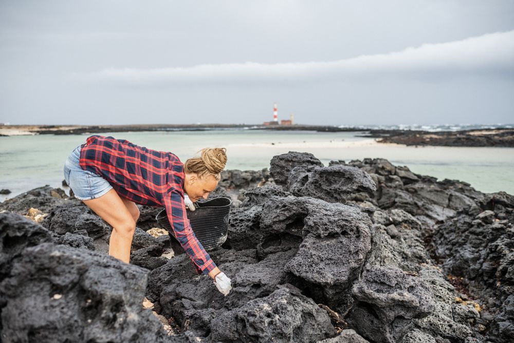 Content modern woman picking litter from sandy seashore