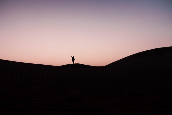 Silhouette of person standing and raising an arm on hill during sunset