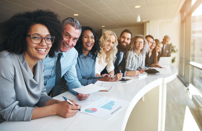Multi-ethnic group of people in office attire standing and smiling in a row at work