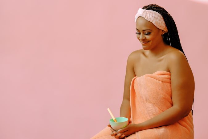 Portrait of woman in spa towel looking down with bowl of product, copy space