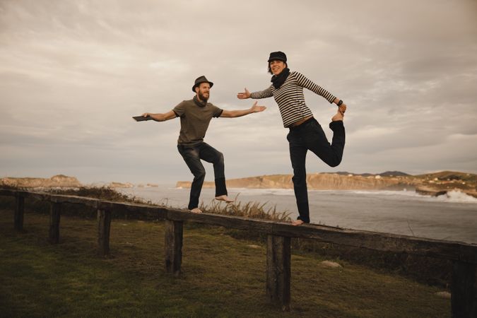 Couple holding hands and jumping on bench on shore near water