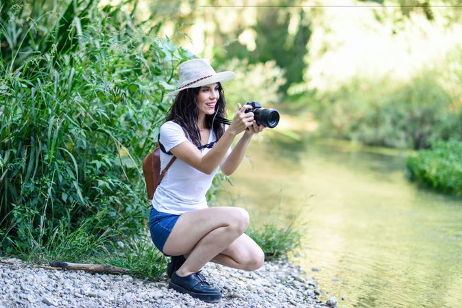 Happy woman sitting with SLR camera near river