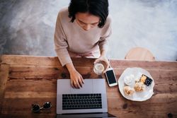Young woman working on a laptop in a coffee shop with a tray of pastries
