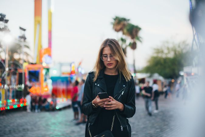 Trendy woman looking down checking phone in fairground