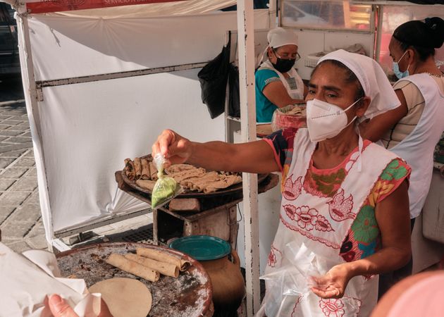 Older woman in facemask preparing food at outdoor stall