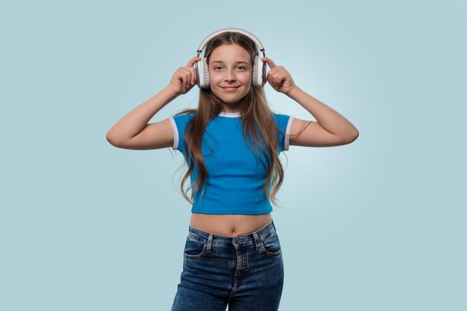 Young girl wearing headphones, smiling while adjusting them.