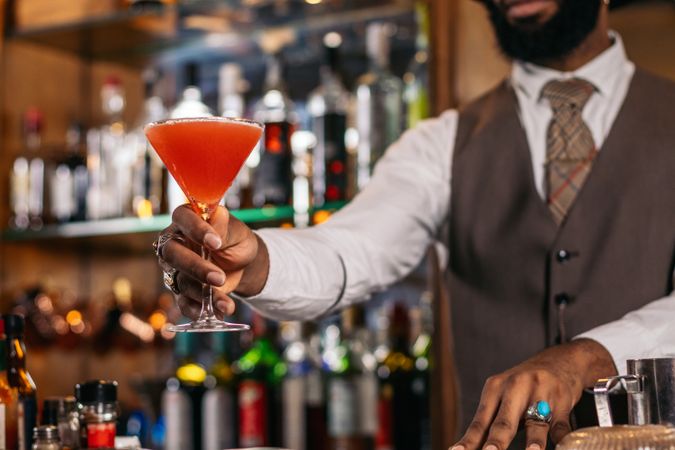 Cutout of a Black bartender offering a cocktail served in a martini glass in a traditional cocktail bar