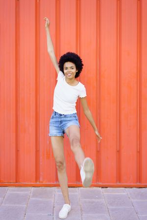 Happy woman standing on one leg with arm up against red background