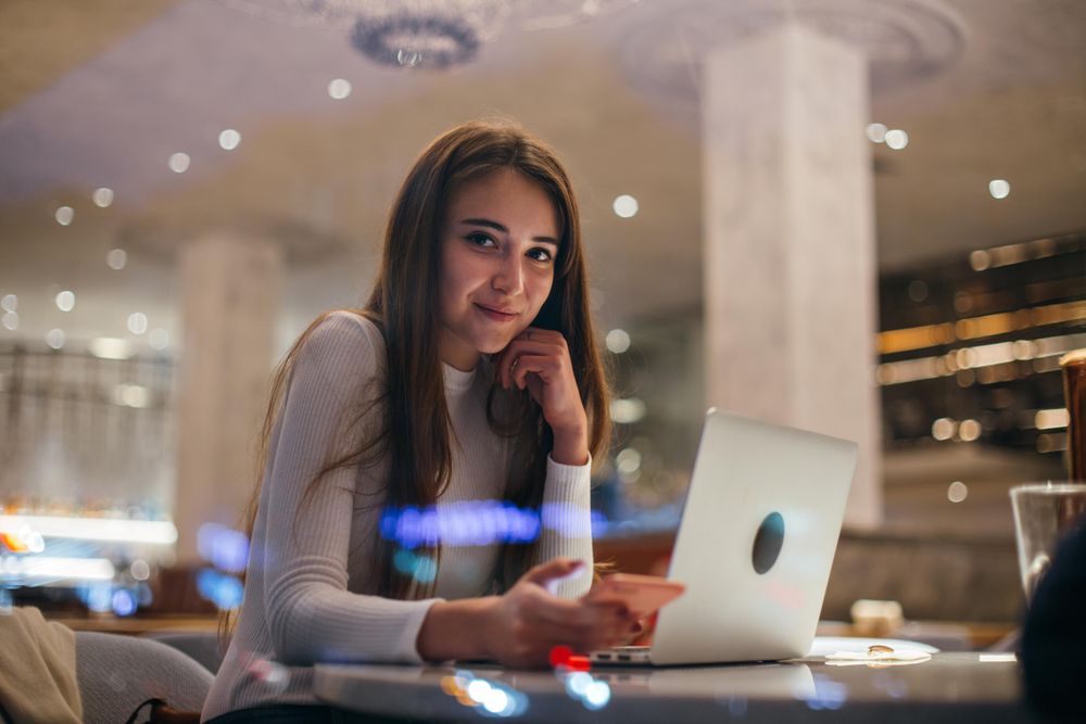 Happy young woman texting in a cafe with laptop in front of her