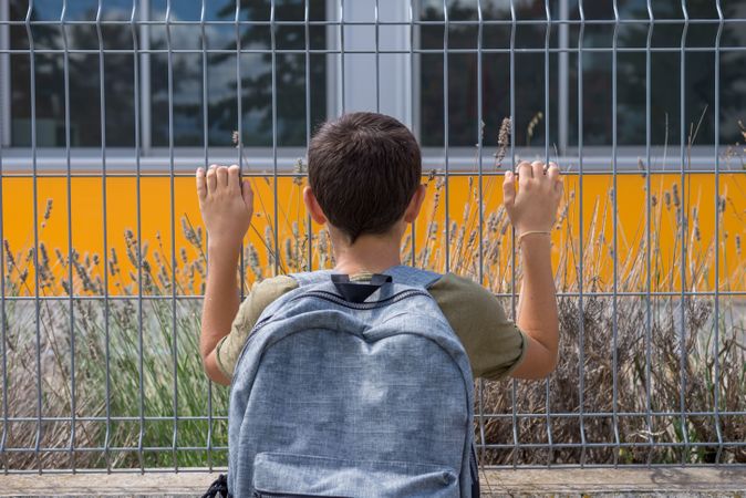 Back of boy with backpack holding fence