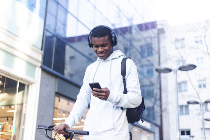 Young Black man biking in the street and checking his phone