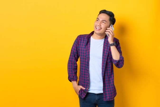 Asian male smiling and talking on cell phone in yellow studio shoot with copy space