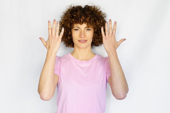 Female in light pink t-shirt standing with hands up with palms facing inwards in blank space