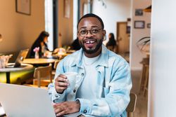 Delighted Black man with coffee browsing laptop