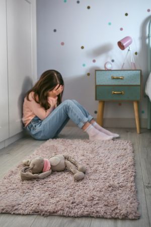 Sad girl with anxiety sitting on the floor of her bedroom with stuffed toy lying