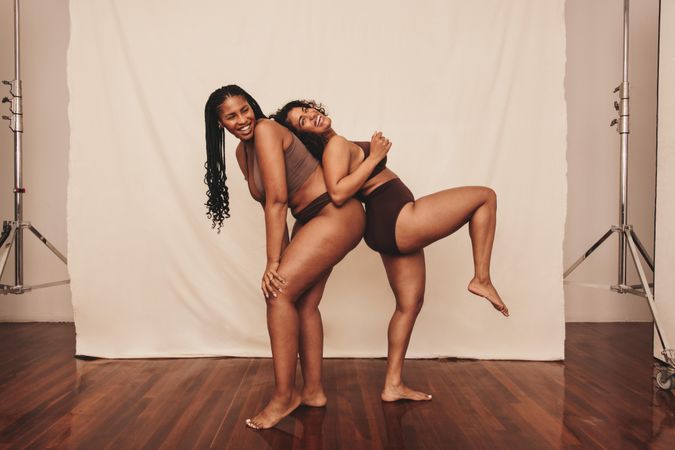 Two happy female friends being playful against a studio background