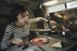 Woman with plate of food near electric cooker in camper van