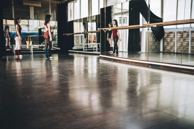 Two young ballerinas in front of big wall mirror training together in studio.